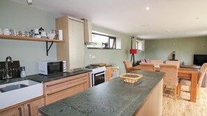 A compact kitchen with a microwave, stove, and sink. A dining area with a table and chairs is visible. - The Owl's Hoot (Tacumshane)