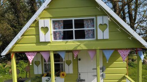 A small, single-story structure with a pitched roof, a front door, and a window with heart-shaped cutouts. - The Owl's Hoot (Tacumshane)