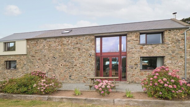 A stone building with a red door, windows, and a bench in the front garden. - The Owl's Hoot (Tacumshane)
