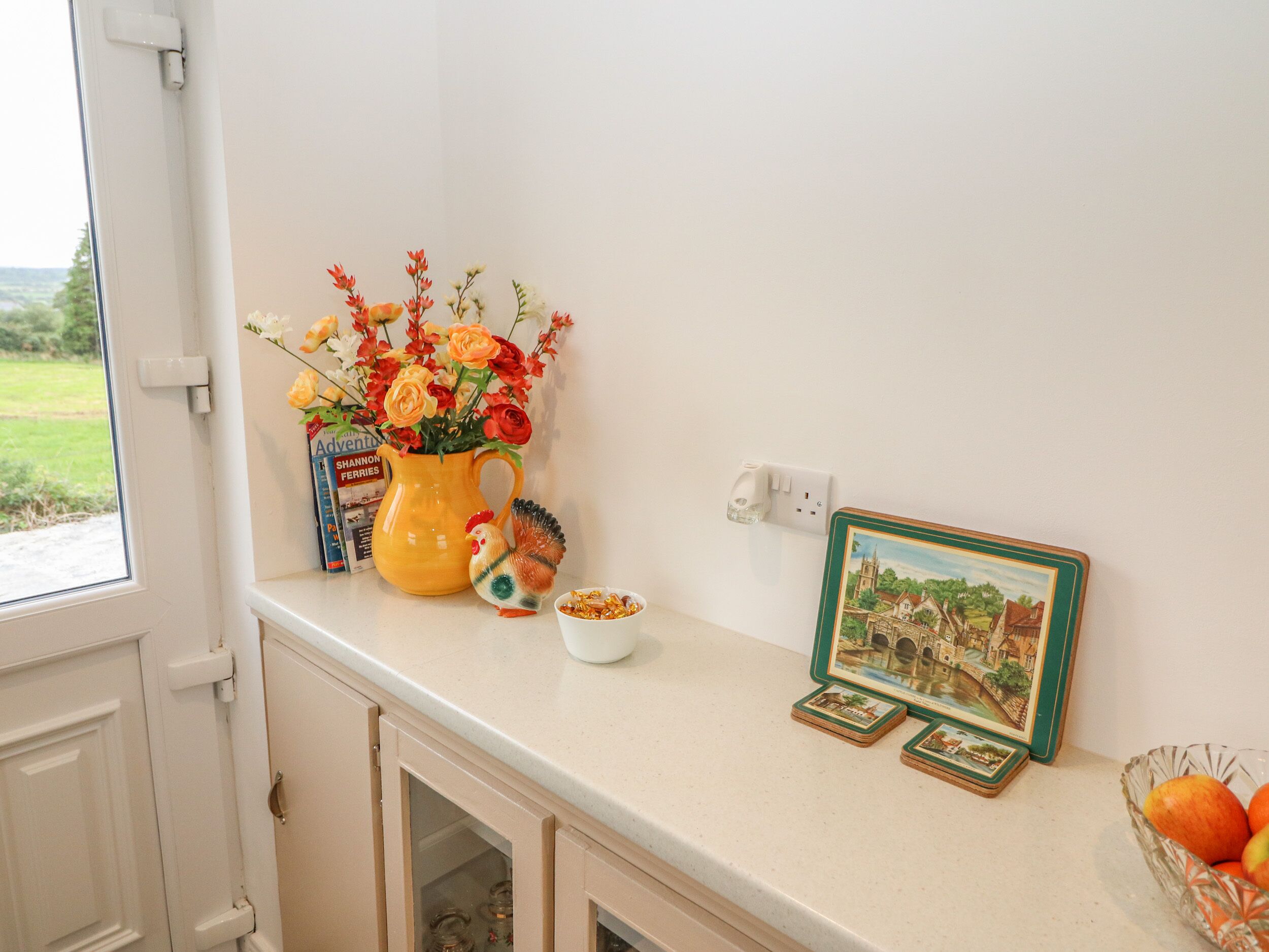 A kitchen counter with a vase of flowers, a rooster figurine, a bowl of snacks, and a framed picture.