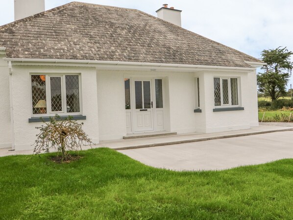 A white single-story house with a grey tiled roof, a front porch, and a small garden.