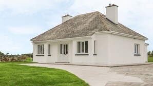 Une maison blanche d’un seul étage, avec un toit recouvert de tuiles, une porte d’entrée et un petit porche.