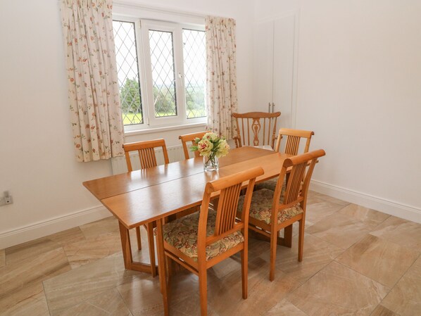A dining area with a wooden table and six chairs, a vase with flowers, and a window with floral curtains.