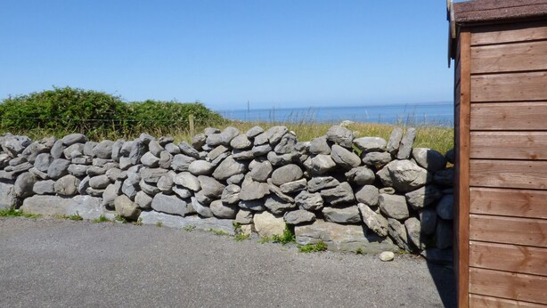 Un muro de piedra con una estructura de madera al lado de una zona pavimentada.