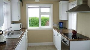A compact kitchen with white cabinets, a microwave, a sink, and a window with a view of greenery. - Ocean View (Ballinskelligs)