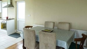 A dining area with a table set for four, a kitchen in the background, and a window providing natural light. - Ocean View (Ballinskelligs)