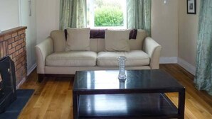 A living room with a beige sofa, a dark wooden coffee table, and a brick fireplace. - Ocean View (Ballinskelligs)