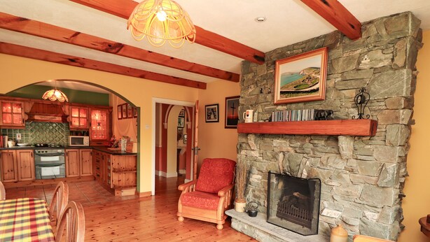 A cozy living room with a stone fireplace, wooden furniture, and a kitchen in the background. - The Lodge (Beaufort)