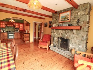 Ein gemütliches Wohnzimmer mit Kamin aus Stein, Holzmöbeln und einer Küche im Hintergrund.