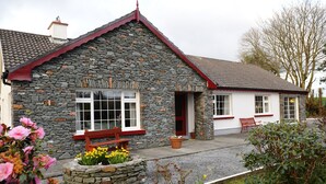 A stone building with a red roof, a bench, and a flower bed in front. - The Lodge (Beaufort)