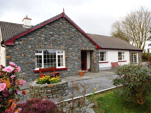 A stone building with a red roof, a bench, and a flower bed in front. - The Lodge (Beaufort)