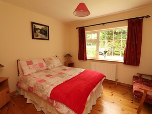 A bedroom with a bed, a window with curtains, a radiator, a bedside table with a lamp, and a picture on the wall. - The Lodge (Beaufort)