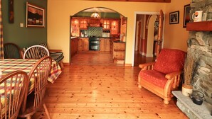 A cozy living room with wooden floors, a dining area with plaid tablecloths, and a kitchen with wooden cabinets and a stone fireplace. - The Lodge (Beaufort)