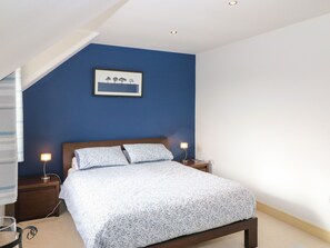 A bedroom with a bed, two bedside tables, a nightstand, a framed picture on the wall, and a staircase.
