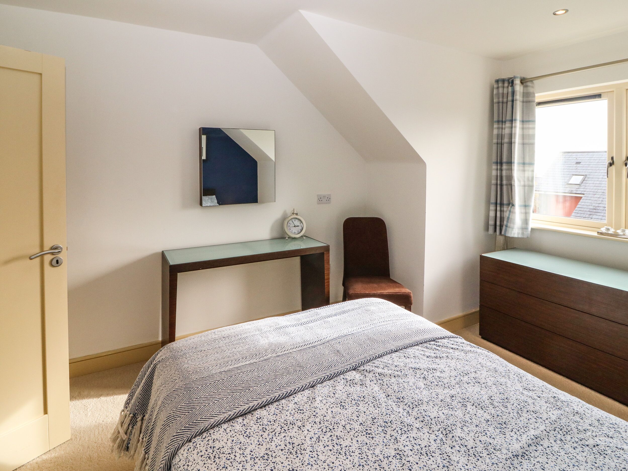 Un dormitorio con cama, escritorio, silla, cómoda, espejo y ventana con cortinas.