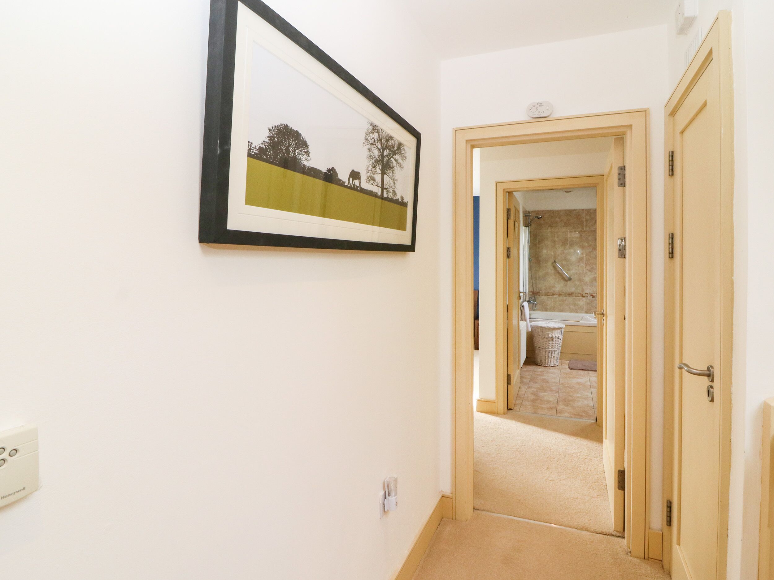 A hallway with a framed picture on the wall, a door leading to a bathroom, and a light switch on the wall.