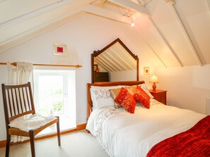Un dormitorio con techo inclinado, estructura de cama de madera, ropa de cama blanca y una manta roja.