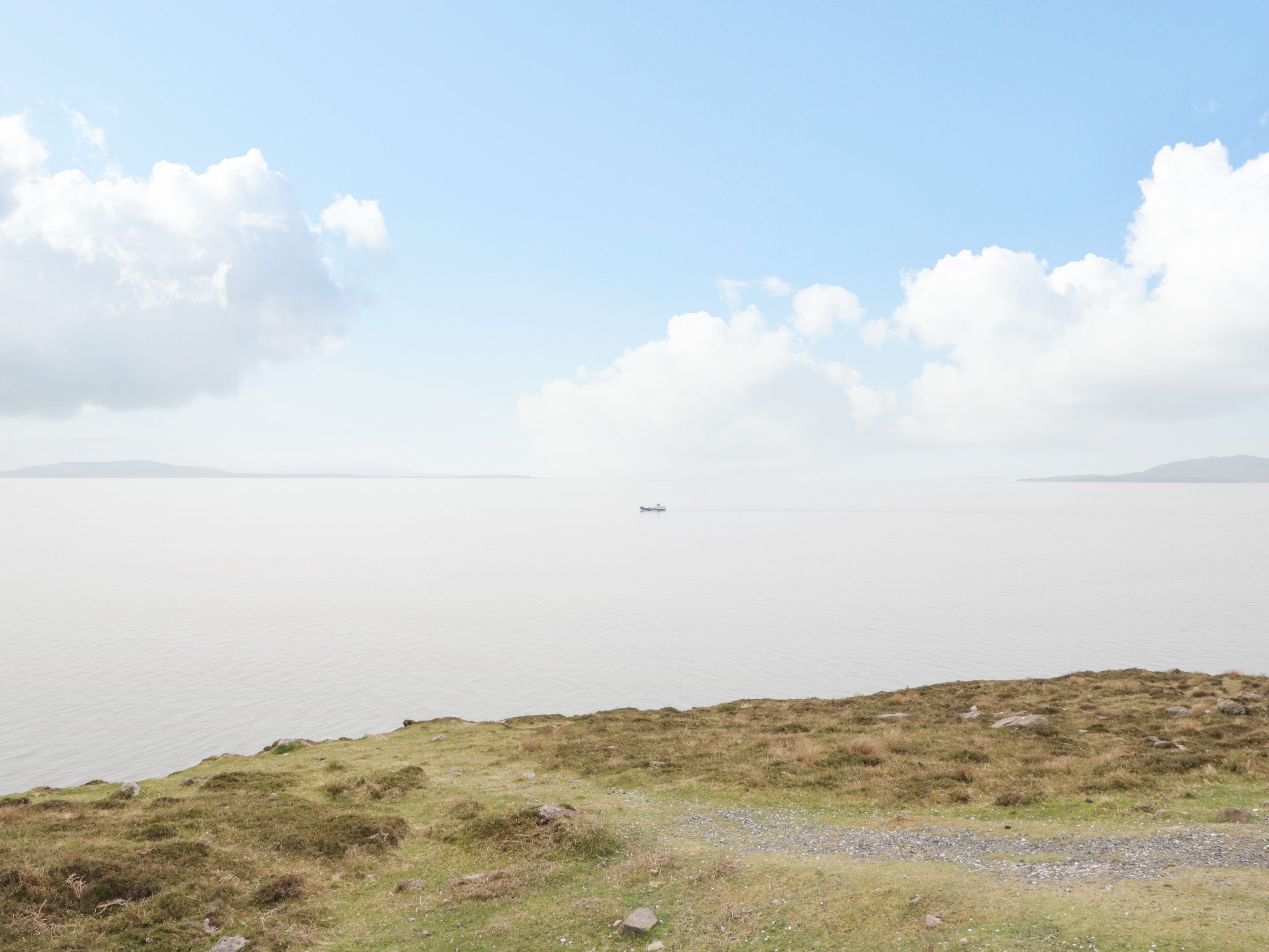 A calm lake with a small boat in the distance, surrounded by grassy hills and a clear sky.