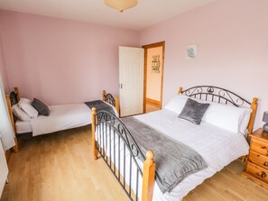 Un dormitorio con dos camas individuales, cabeceros de madera, un aparador de madera y una puerta que da a otra habitación.