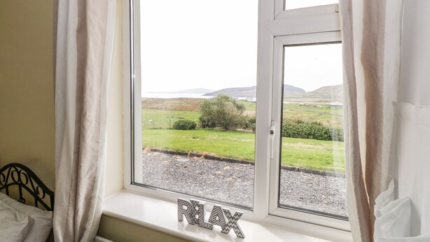 A room with a window overlooking a rural landscape, a radiator below the window, and a bed to the left.