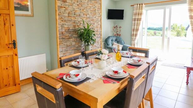 A dining area with a wooden table set for four, a potted plant, and a television on the wall. - Artigallivan (Killarney)