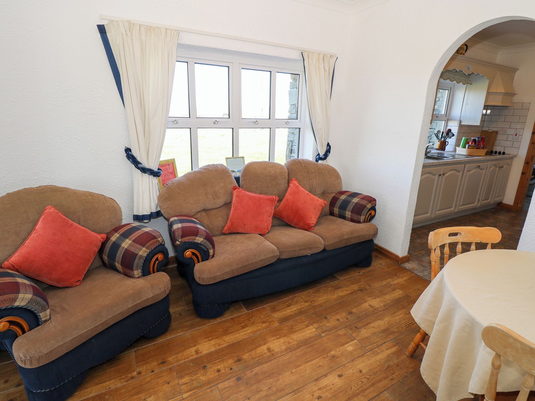 A cozy living room with a sofa set, a dining table, and a kitchen visible through an archway.