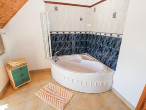 A corner bathroom with a freestanding bathtub, a wooden cabinet with drawers, a towel rack, and a patterned rug.