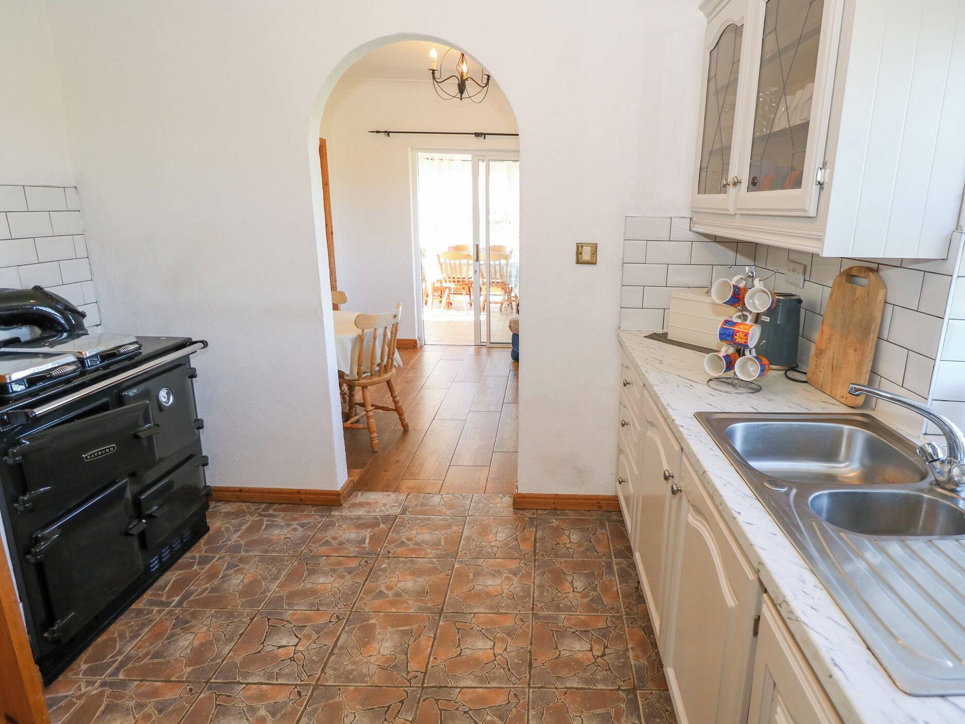 A kitchen with a stove, sink, and cabinets. There is a dining area with chairs and a table visible through an archway.