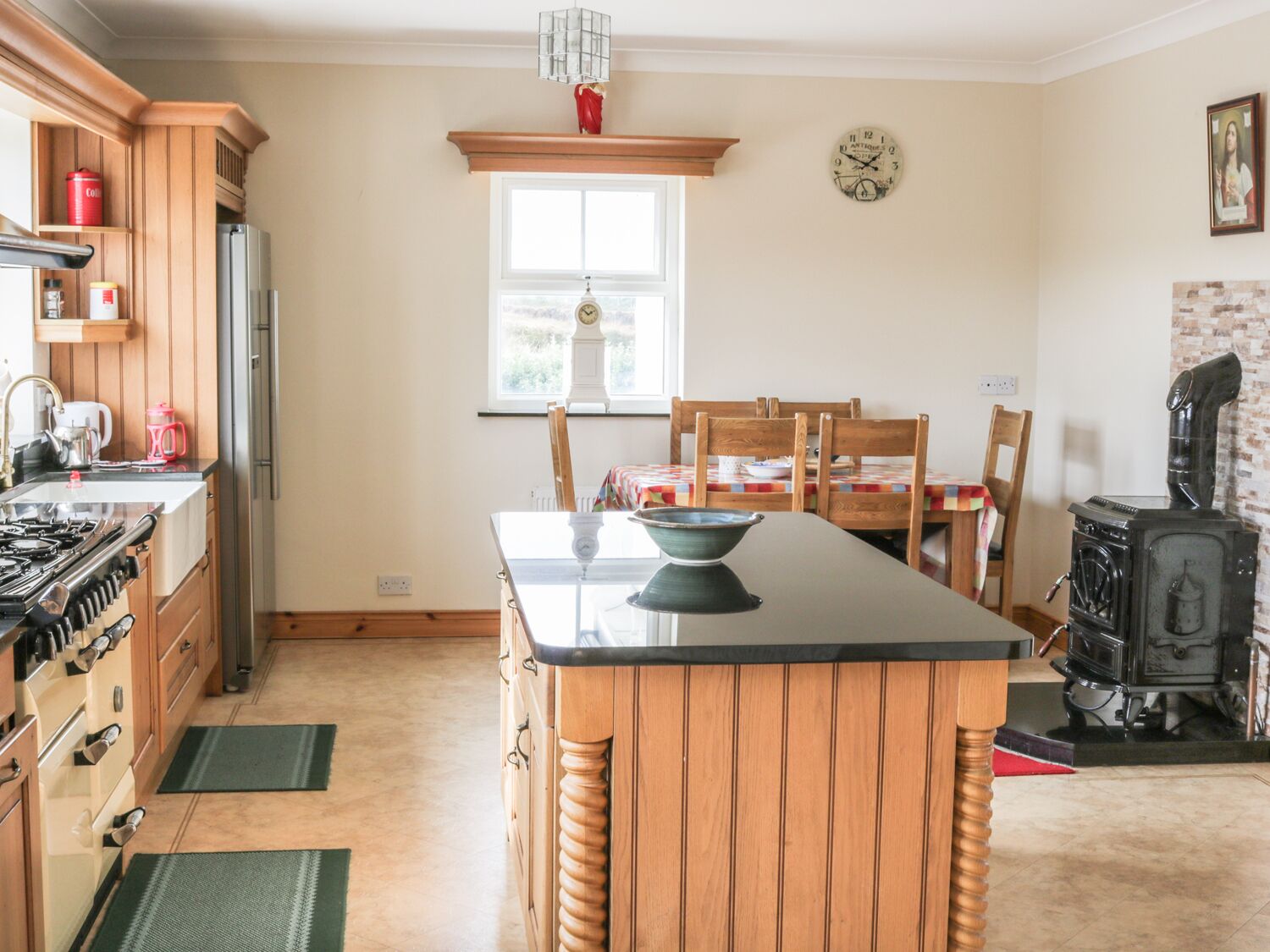 A kitchen with wooden cabinets, a gas stove, a refrigerator, a dining table with chairs, a clock, and a vintage stove.