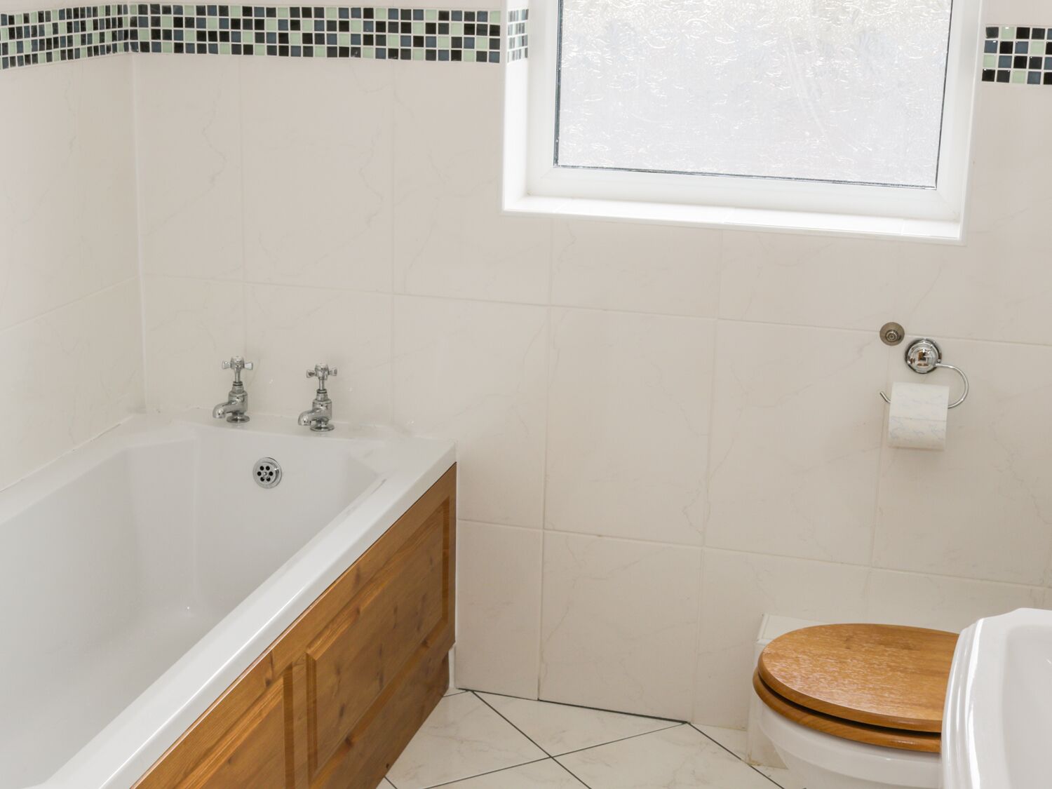 Een badkamer met een bad, houten wastafelmeubel, toilet en een raam.