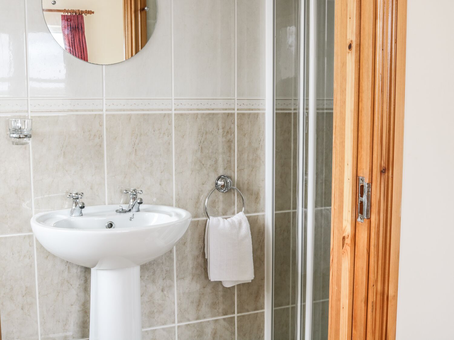 Un baño con lavamanos blanco de pedestal, un espejo y una cabina de ducha de vidrio.