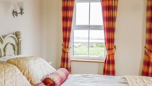 A bedroom with a bed, a headboard, a window with curtains, and a wall-mounted light fixture.