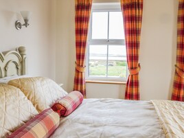 Un dormitorio con una cama, cabecera, ventana con cortinas y una lámpara fijada a la pared.