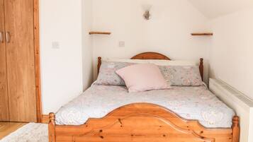 Un letto di legno con biancheria da letto floreale, un armadio di legno e un termosifone bianco.