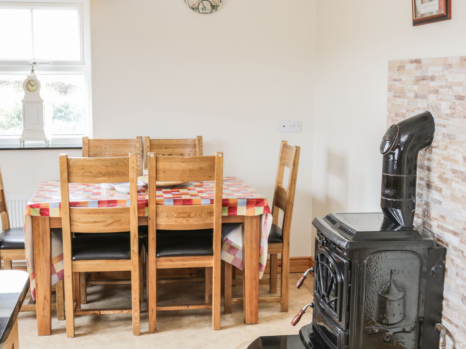A dining area with a wooden table and chairs, a vintage stove, and a window with a clock.