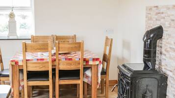 A dining area with a wooden table and chairs, a vintage stove, and a window with a clock.
