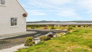 A white building with a gravel driveway and a grassy area with shrubs.