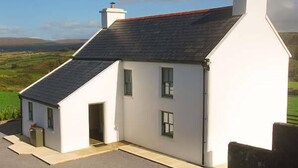 A white house with a steeply pitched roof, a chimney, and a small porch area. - Nellie's Farmhouse (Bantry)