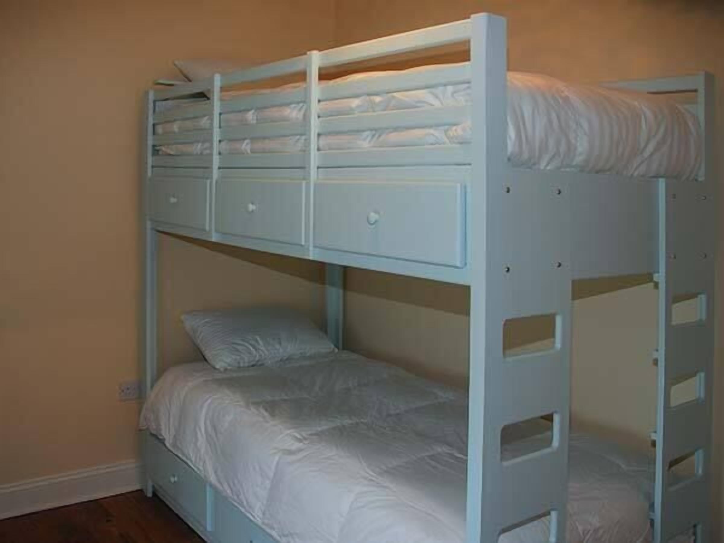 Una cama litera con escalera y cajones, en una habitación con paredes color crema.