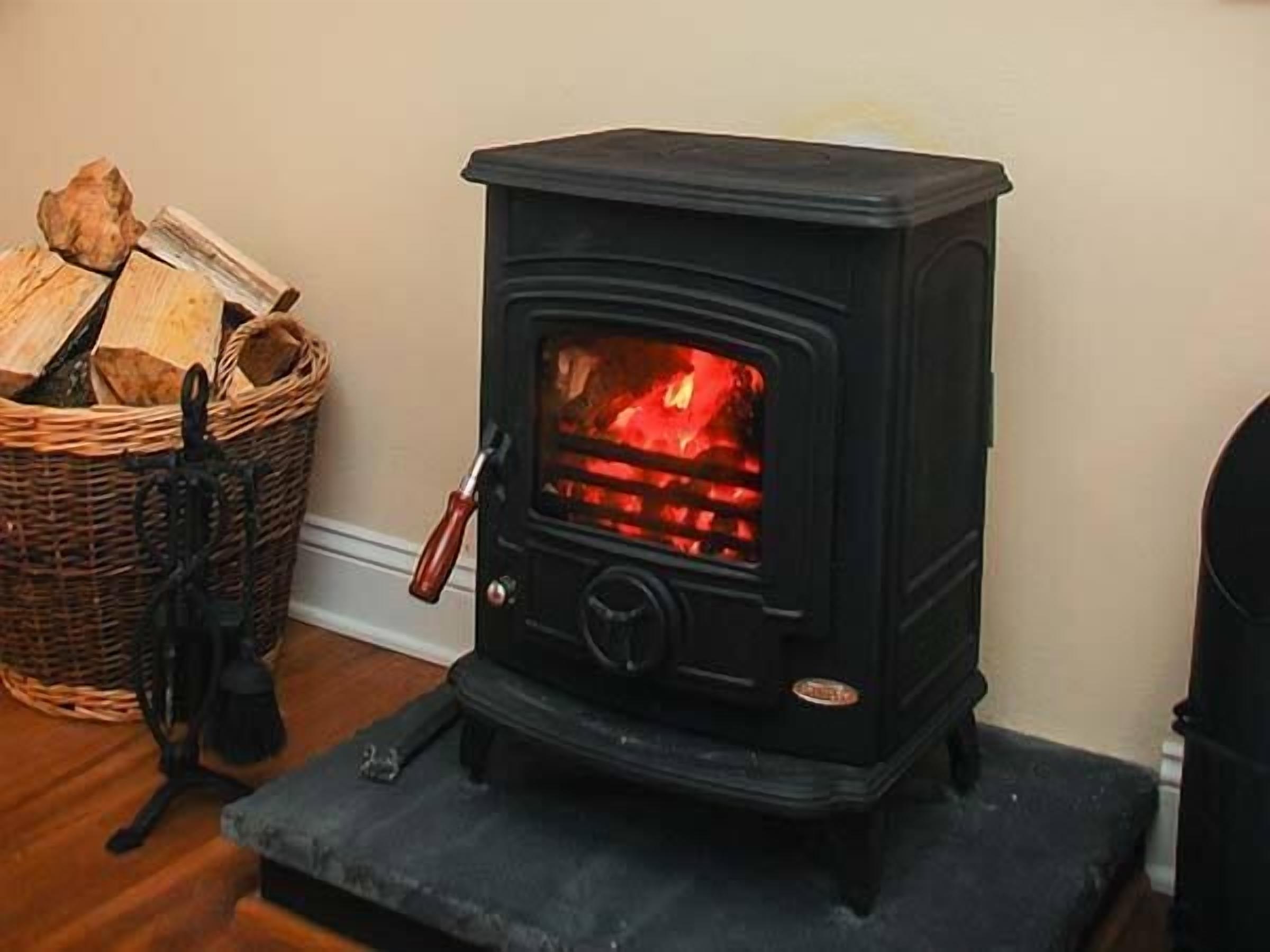 A wood-burning stove with logs in a basket beside it.