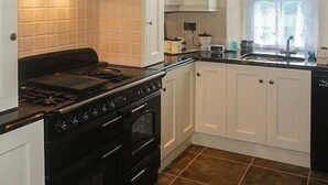 A kitchen with white cabinets, a black stove, and a window with curtains. - Nellie's Farmhouse (Bantry)