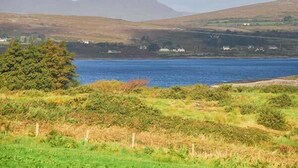 A coastal landscape with a body of water, hills, and sparse vegetation. - Nellie's Farmhouse (Bantry)