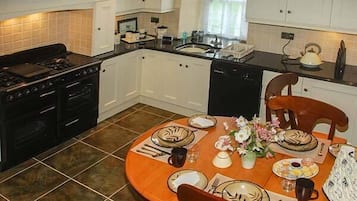 A modern kitchen with white cabinets, a black stove, and a dining table set for four with plates, cutlery, and a vase of flowers.