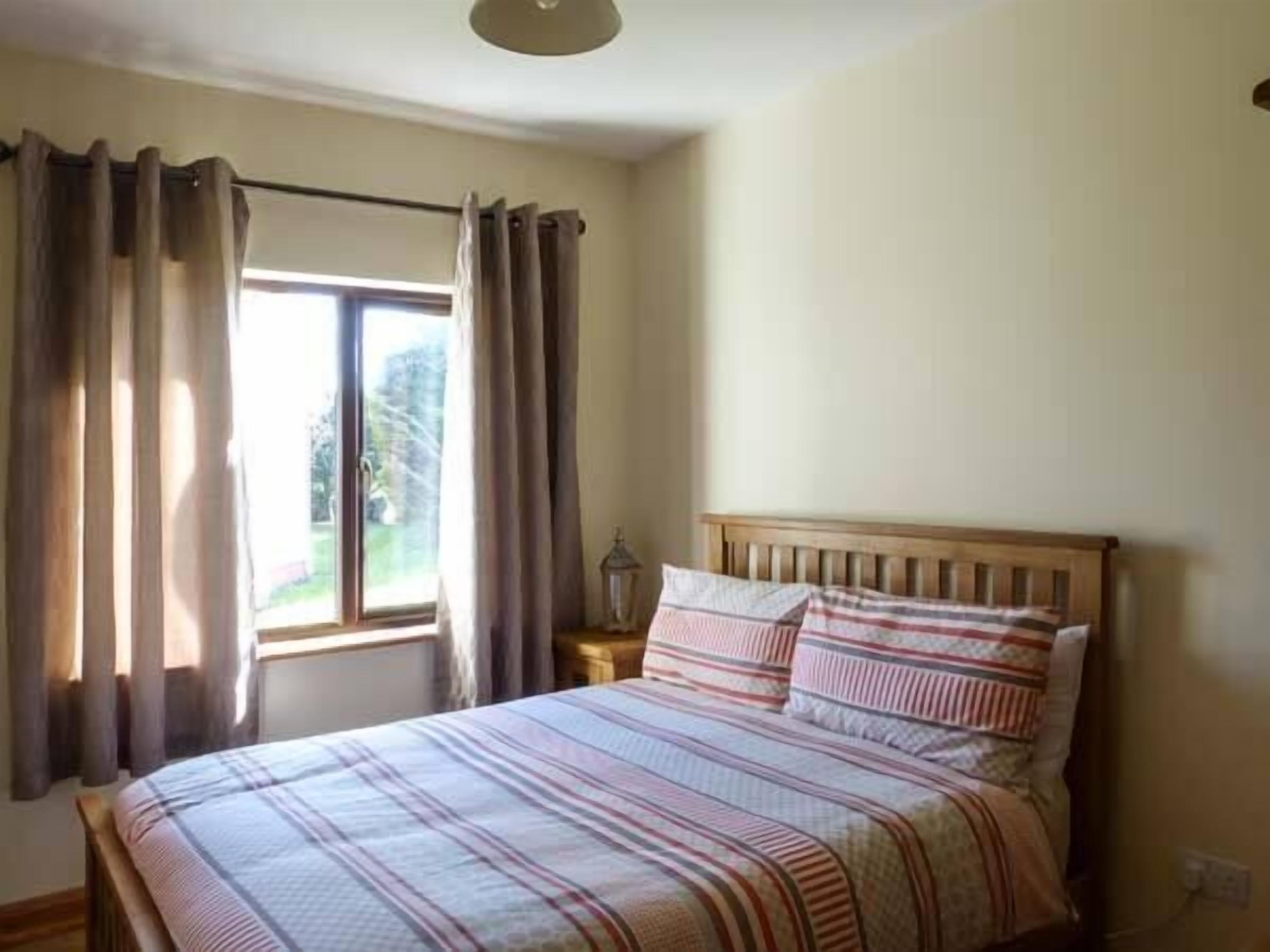 A bedroom with a bed, curtains, a window, and a nightstand.