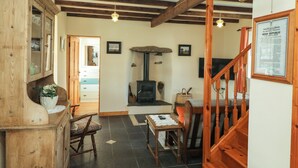 Un intérieur rustique avec des poutres apparentes, une cheminée, un escalier en bois et un meuble traditionnel.