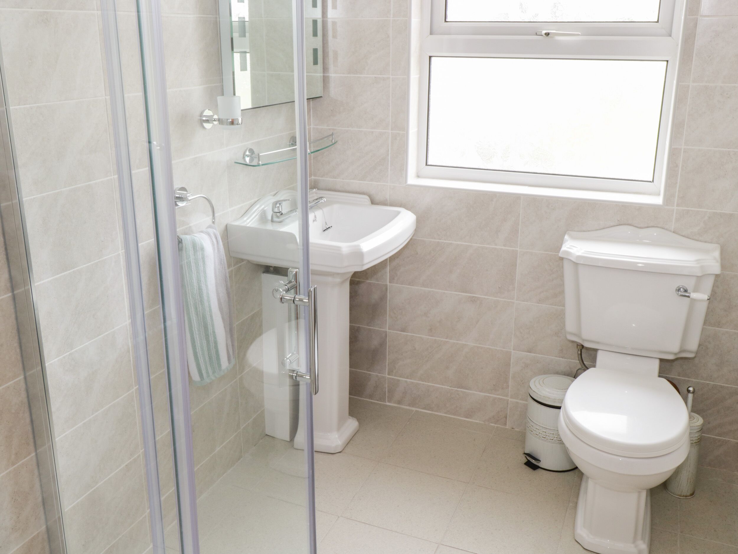 A bathroom with a glass shower enclosure, a pedestal sink, and a toilet.