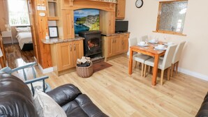 A cozy living room with a fireplace, wooden cabinets, a dining table set for four, and a comfortable sofa. - Cherry Tree Cottage (Ballintober)