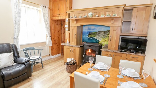 A cozy living room with a fireplace, wooden cabinets, a dining table set for four, and a comfortable leather sofa. - Cherry Tree Cottage (Ballintober)