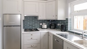 A modern kitchen with white cabinets, a stainless steel refrigerator, a dishwasher, and a window providing natural light. - Cherry Tree Cottage (Ballintober)