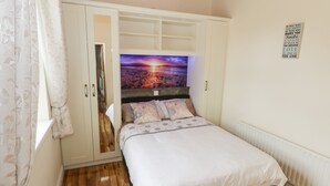 A bedroom with a bed, a wardrobe, a wall with a poster, and a window with curtains. - Cherry Tree Cottage (Ballintober)